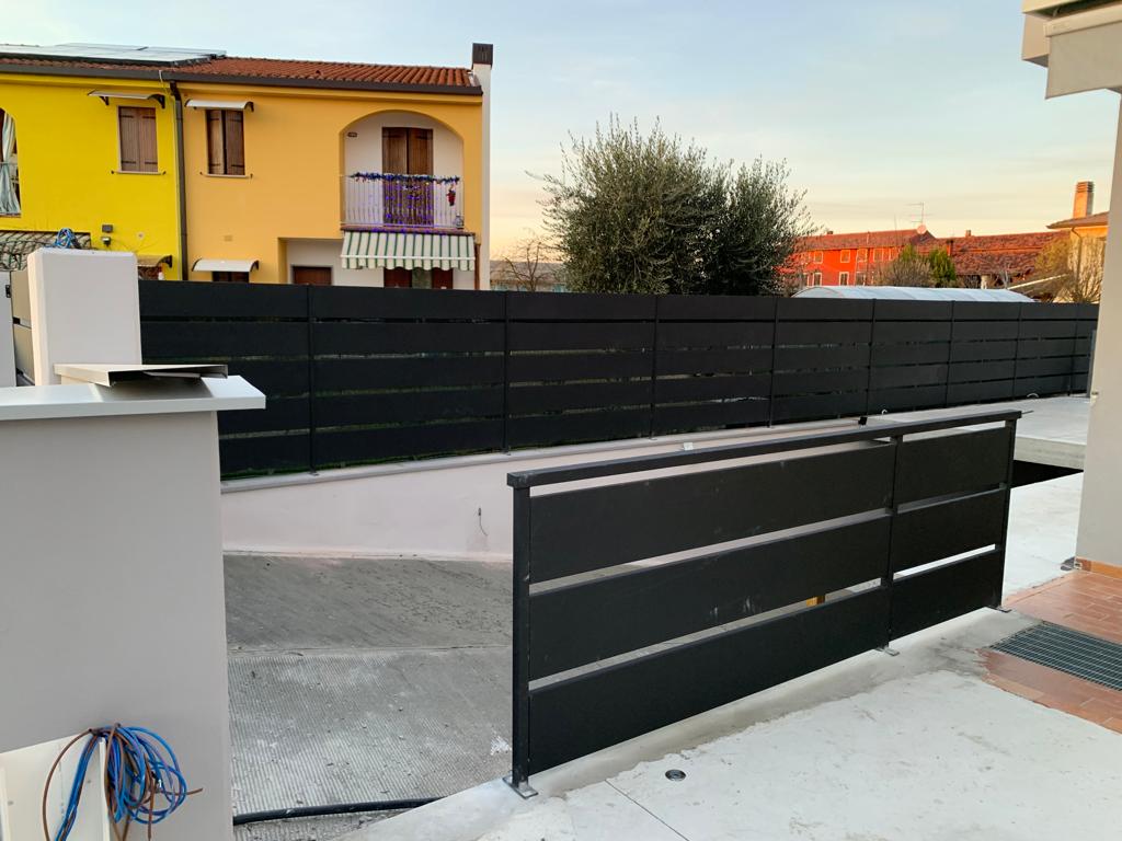 Recinzione e cancello neri con listelli orizzontali davanti agli edifici.