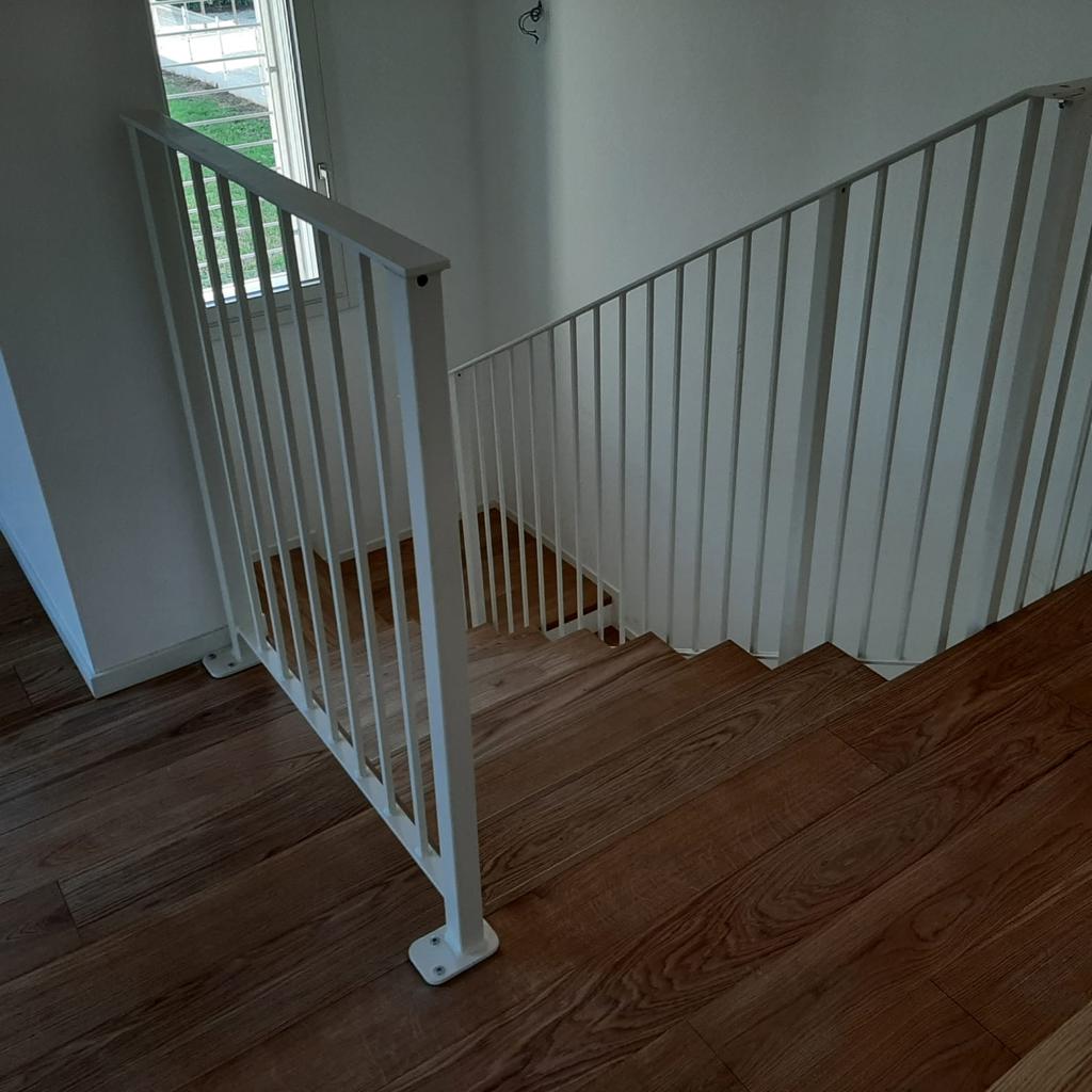 Scala con ringhiera bianca e gradini in legno. La luce del sole entra a fiotti da una finestra.