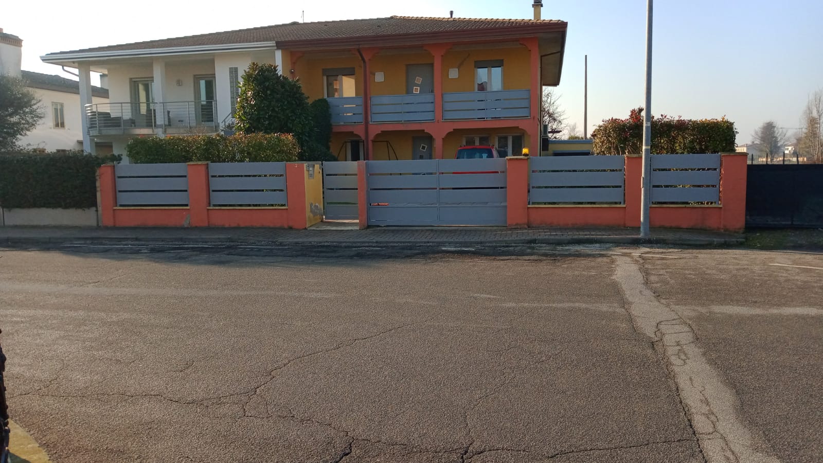Casa arancione con recinzione e cancello grigi su una strada asfaltata.