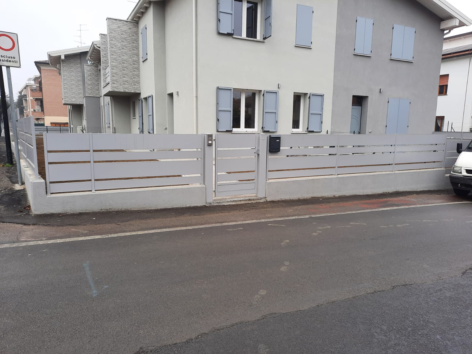 Casa grigia con recinzione e cancello coordinati lungo una strada asfaltata.