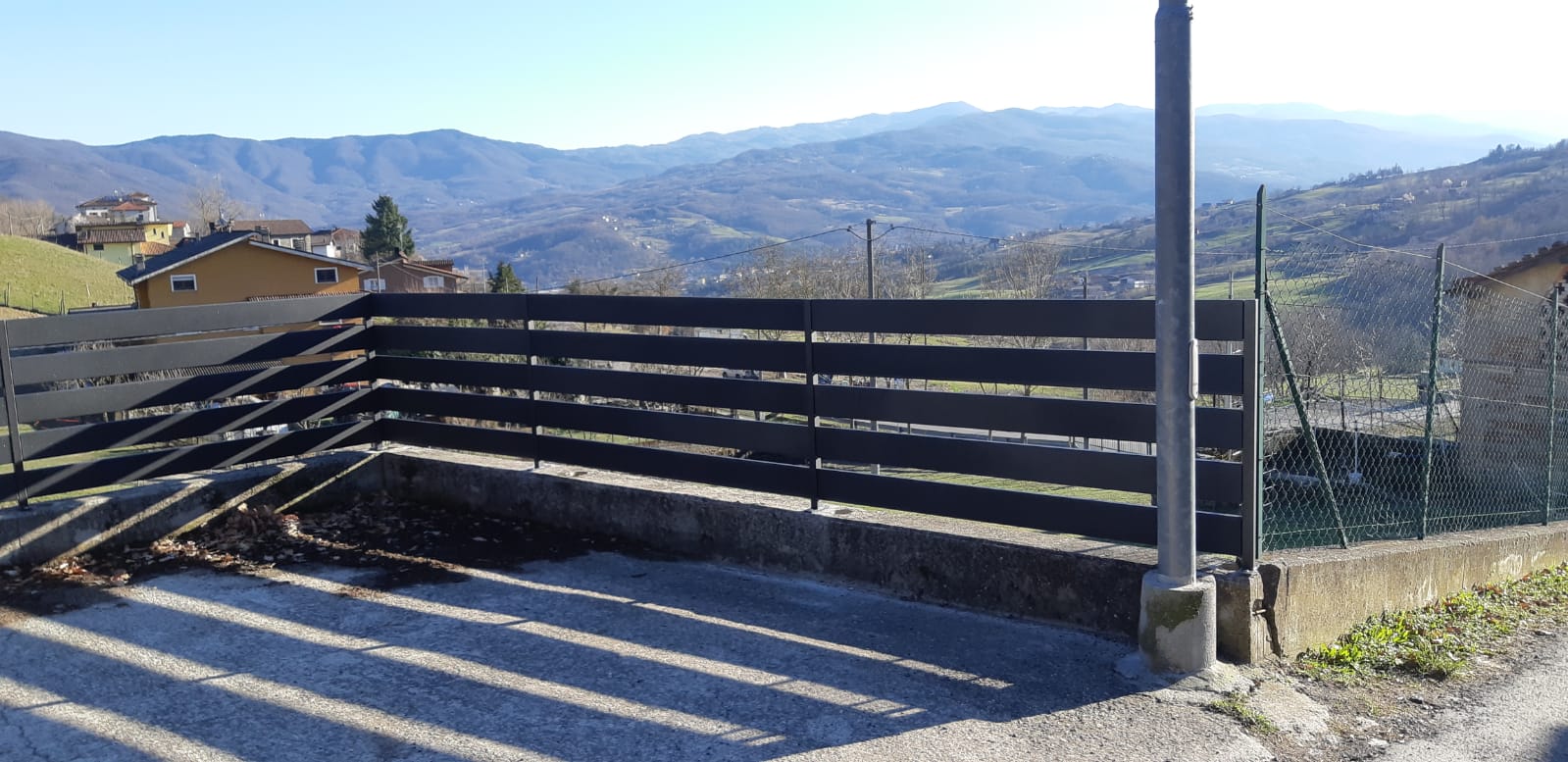 Recinzione in legno scuro con catena montuosa sullo sfondo in una giornata di sole.