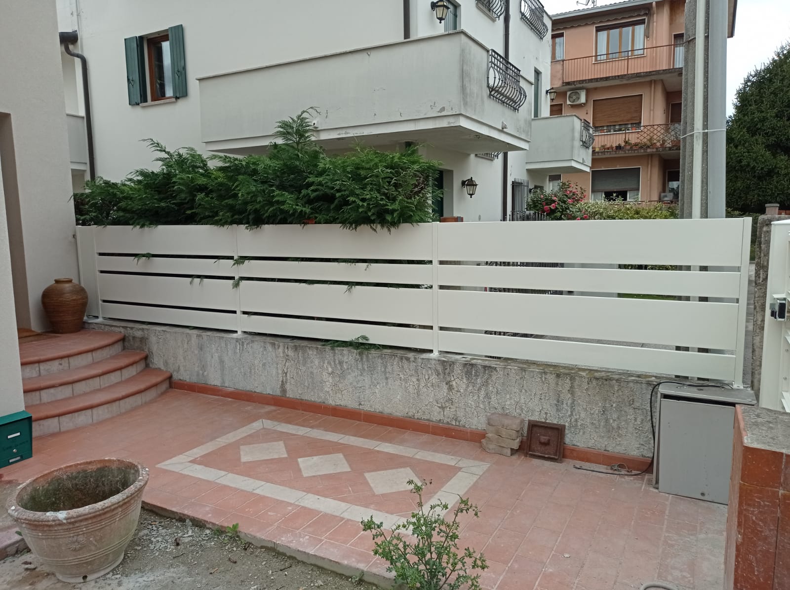 Recinzione bianca a doghe orizzontali davanti a un edificio con terrazza e gradini.