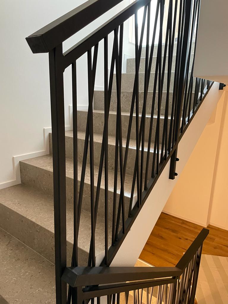 Scala con ringhiera in metallo nero e gradini in cemento grigio chiaro.