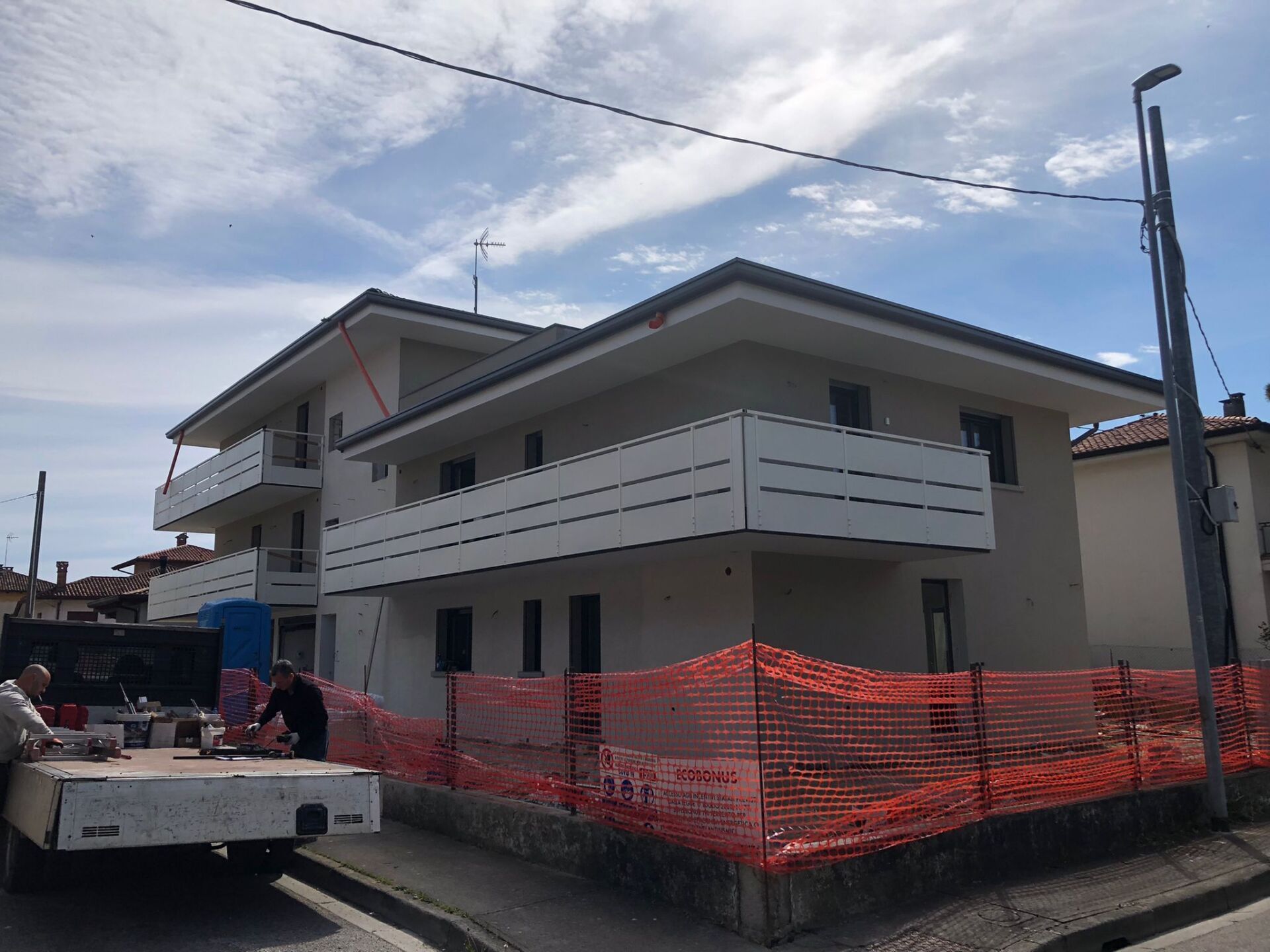 Edificio a due piani in costruzione con balconi bianchi, circondato da recinzioni di sicurezza arancioni.