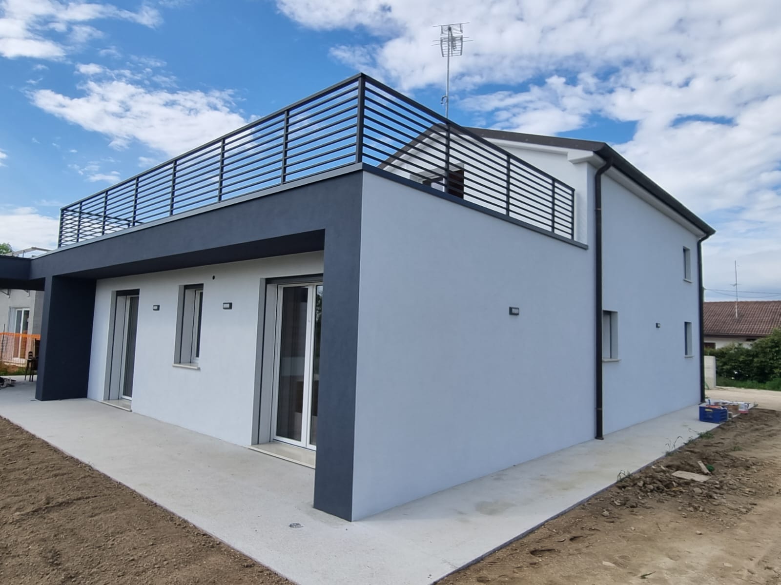 Moderna casa a due piani con dettagli grigi, balcone e ringhiera scura. Pareti bianche, cielo azzurro.