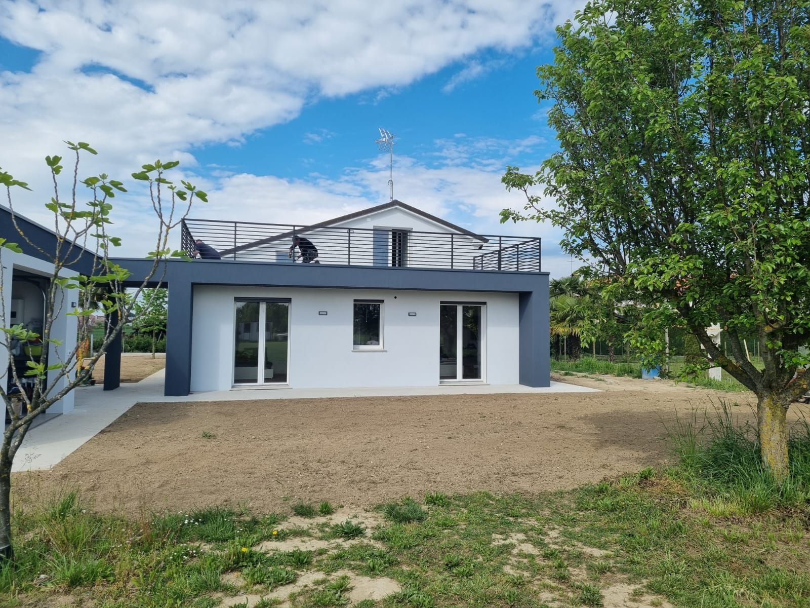 Moderna casa bianca con tetto piatto e finiture grigio scuro, sotto un cielo azzurro.