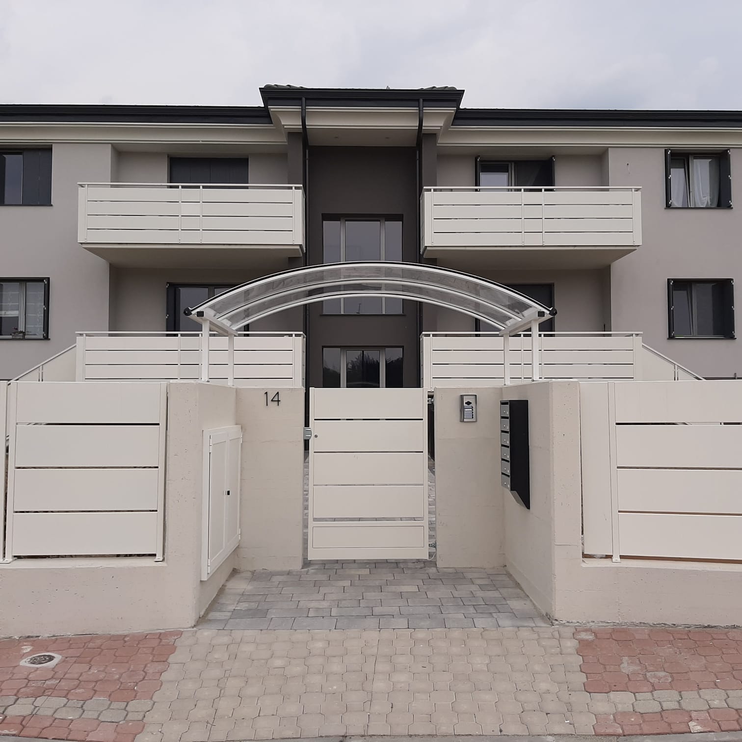 Un condominio a due piani con balconi, ingresso con cancello e una tenda trasparente sopra la porta.