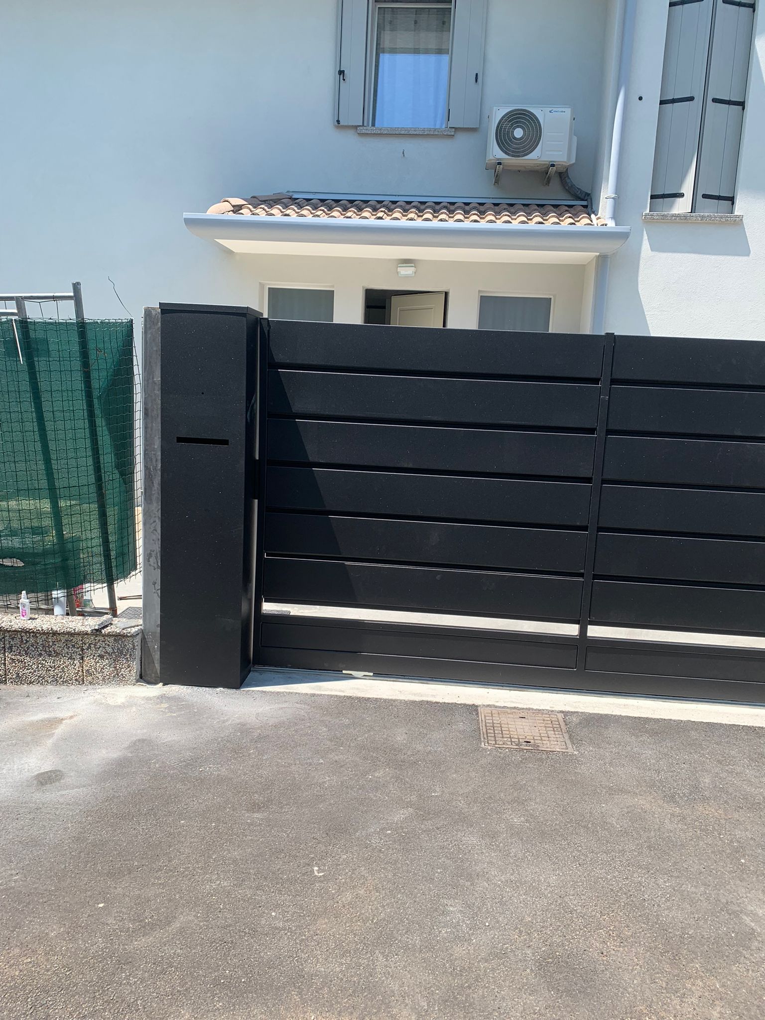 Cancello orizzontale nero con cassetta della posta, di fronte a una casa bianca.