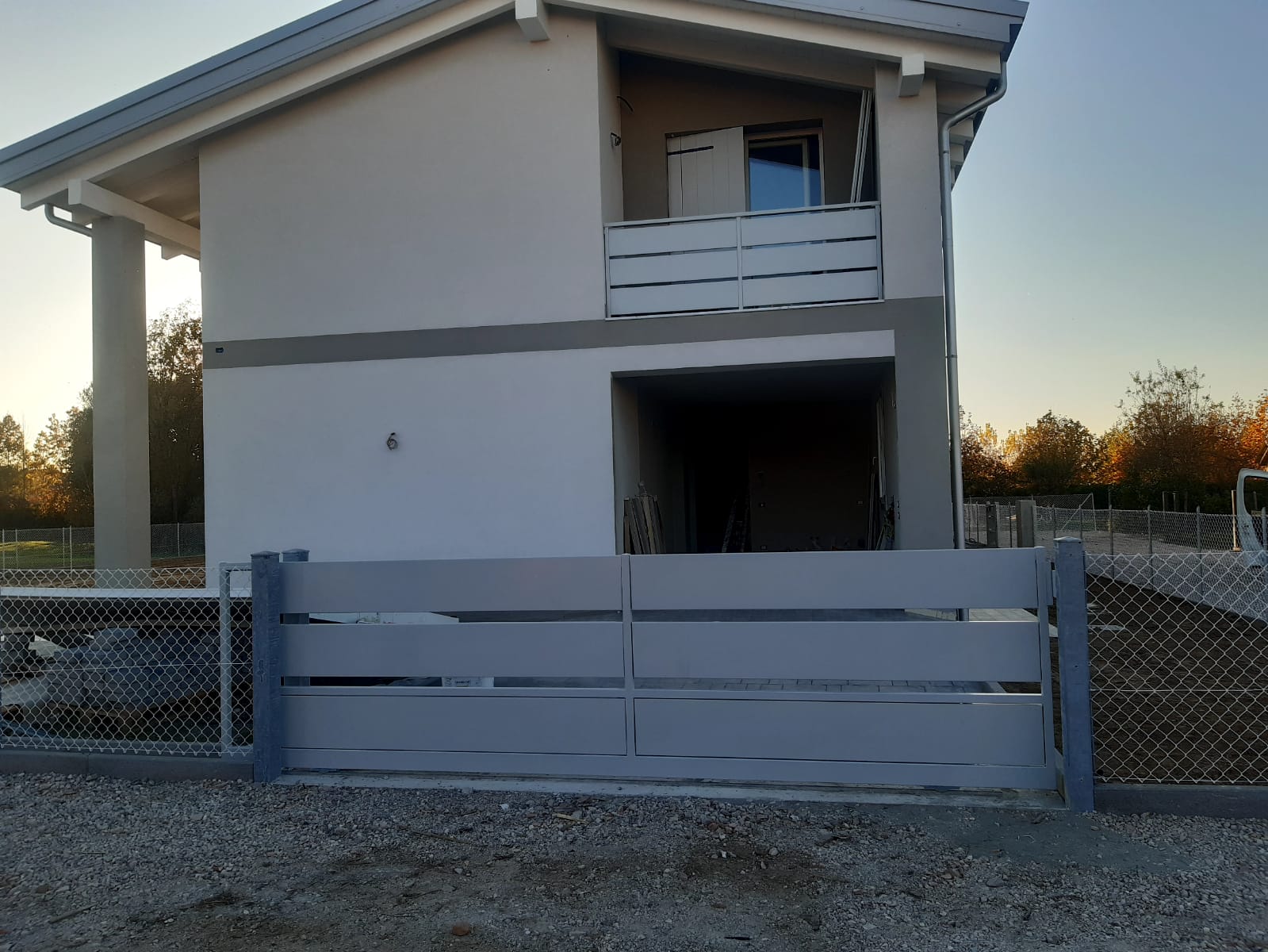 Casa grigia con cancello grigio, vialetto di ghiaia e recinzione a maglie di catena.