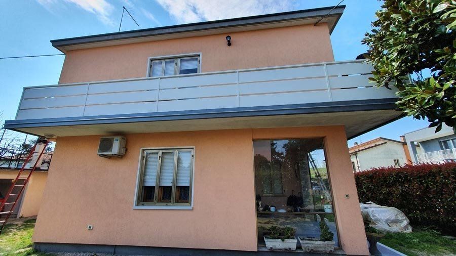 Edificio color pesca a due piani con balcone e porta in vetro, cielo azzurro sullo sfondo.