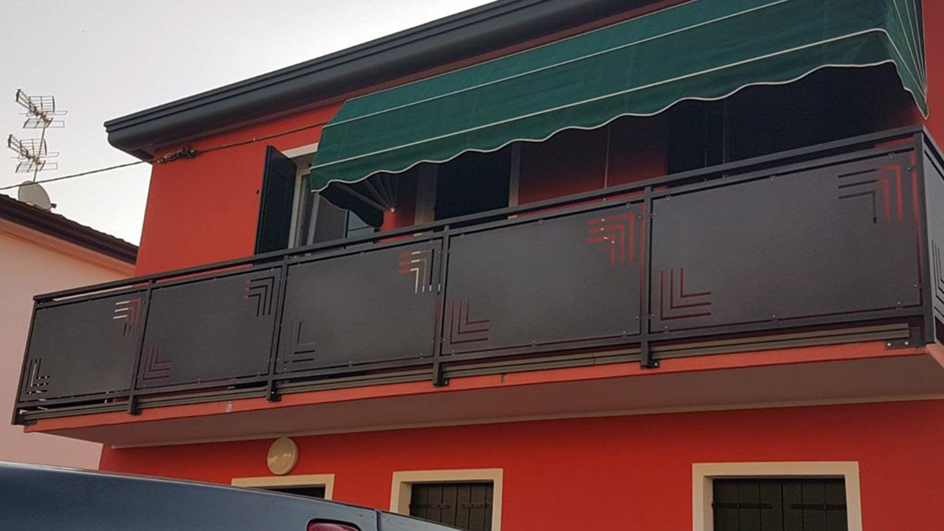 Edificio rosso con balcone caratterizzato da una ringhiera nera e una tenda da sole verde.