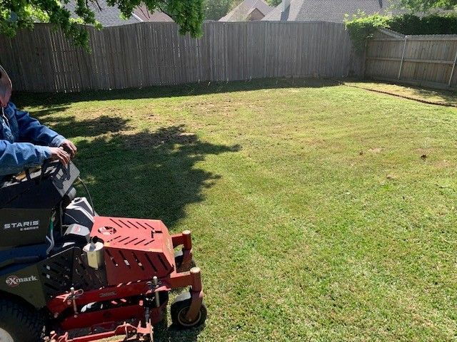 A person on a red riding lawnmower cutting grass in a backyard with a wooden fence.