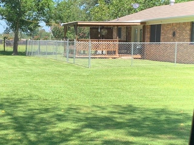 Lush green lawn with a chain link fence surrounding a wooden patio attached to a brick house.