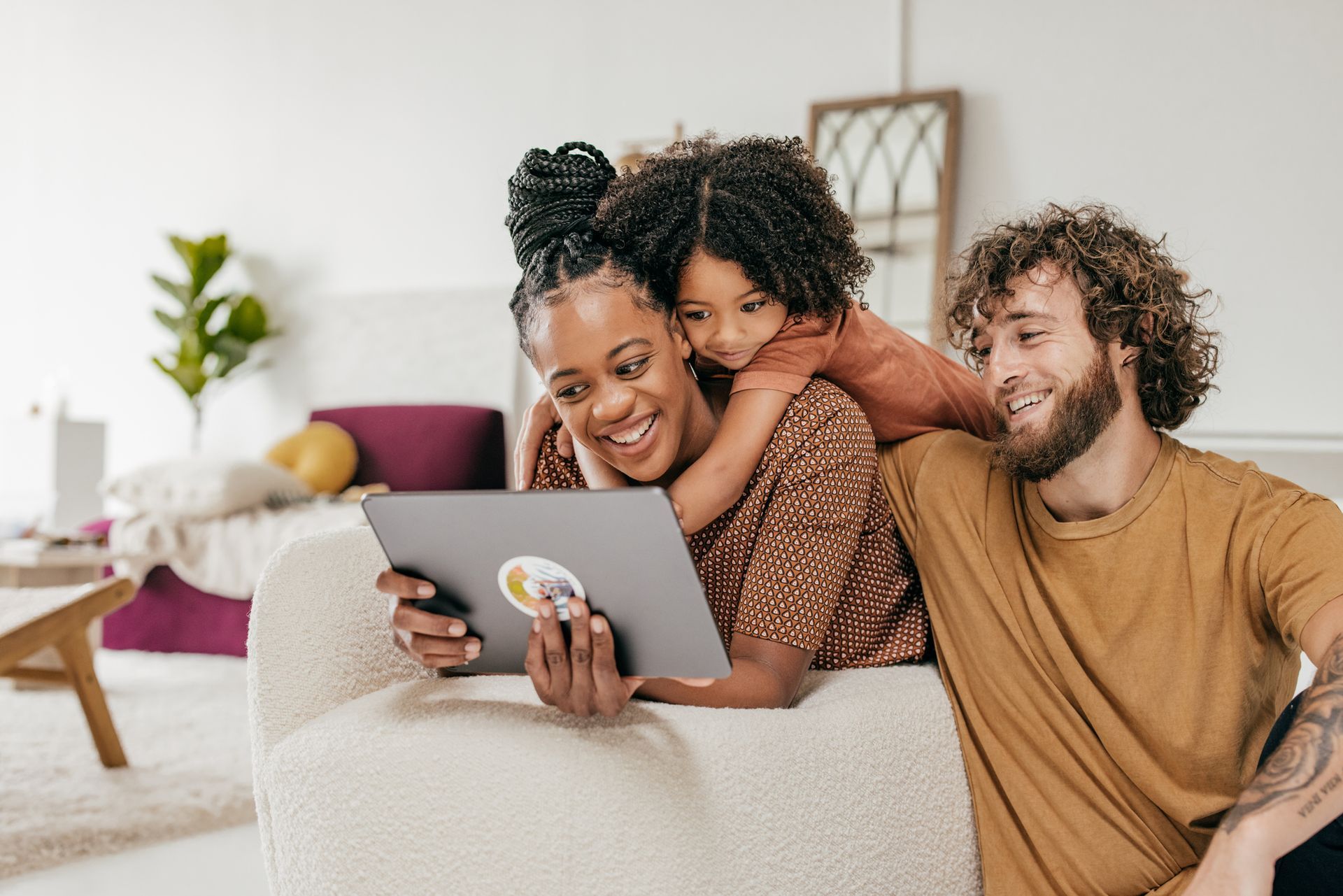A family is sitting on a couch looking at a tablet.