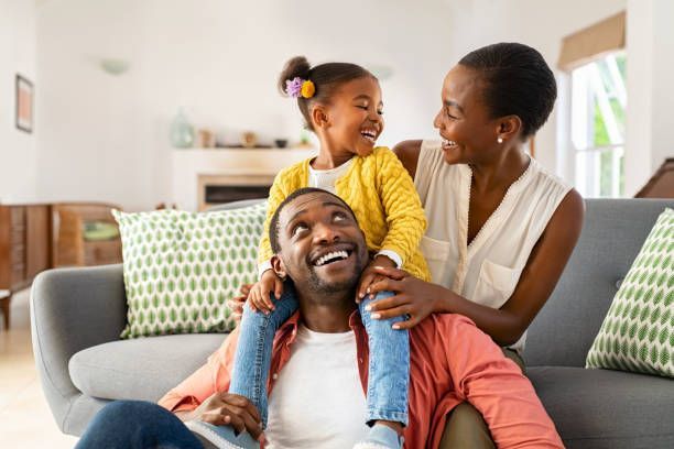 A man and woman are sitting on a couch with a little girl on their shoulders.