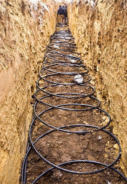 A man is standing in a trench with a bunch of pipes in it.