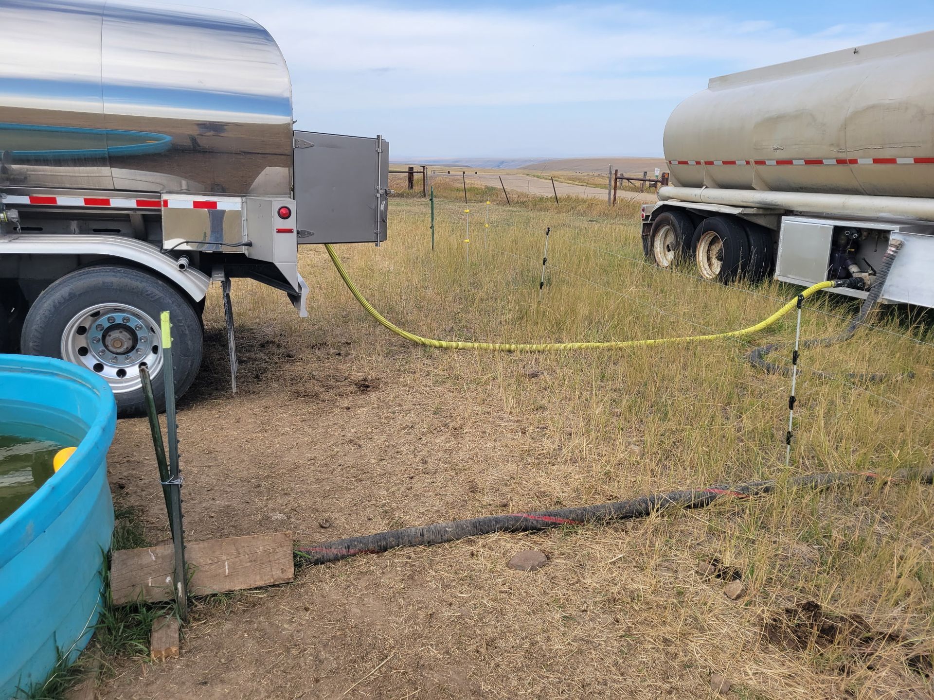 Two tanker trucks connected by a yellow hose, possibly transferring liquid. Outdoors, on dry land.