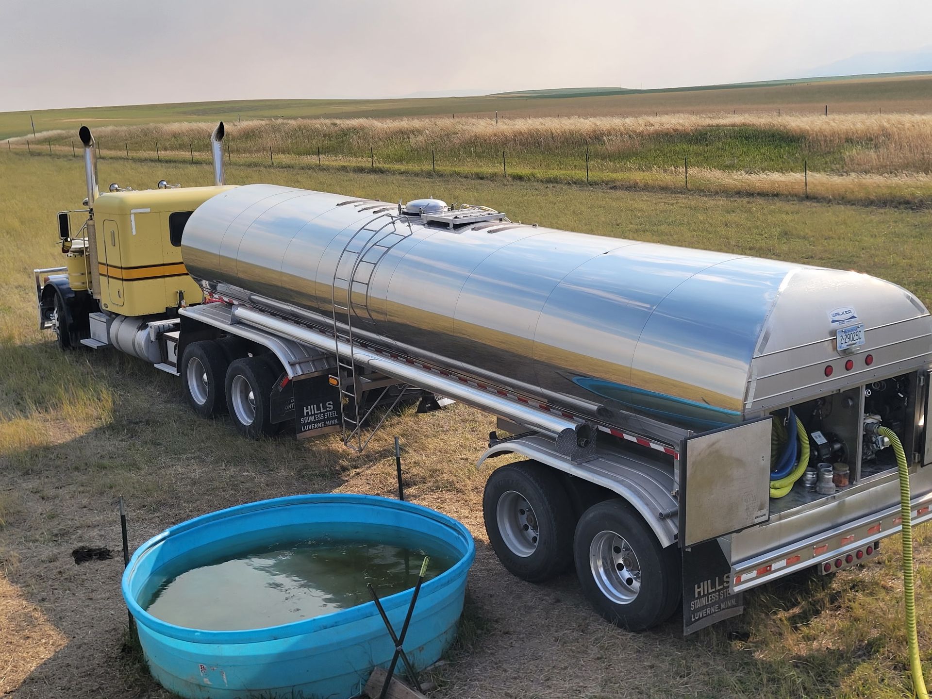 Yellow tanker truck filling a water trough in a rural setting.