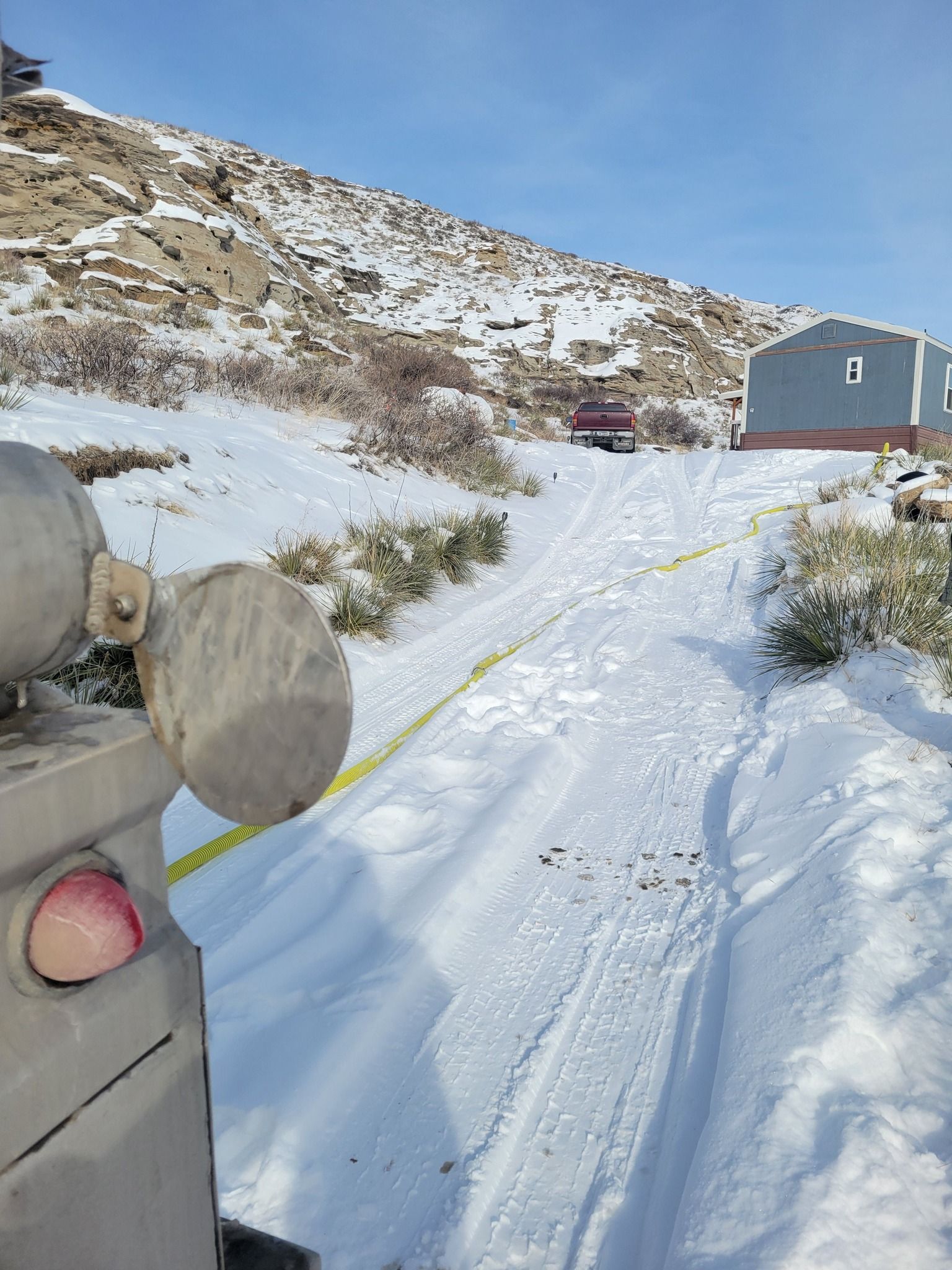 Snowy scene with vehicle, caution tape, and building on a hillside.