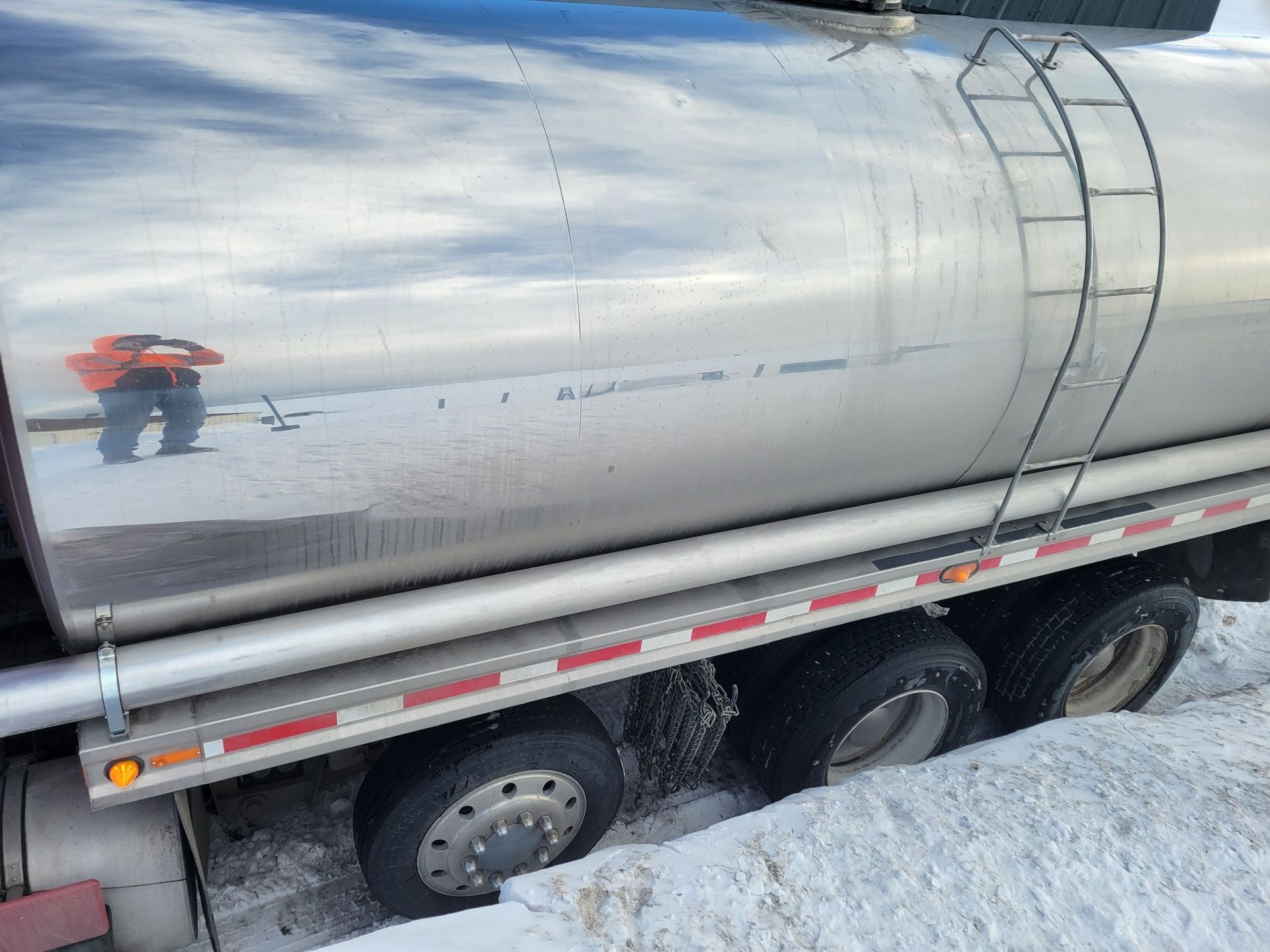A tanker truck stuck in deep snow, with a person visible on the ground in the background.
