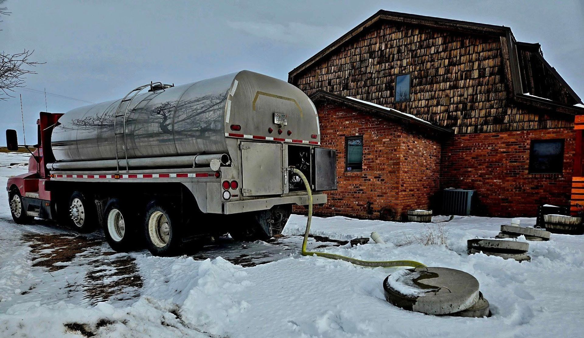 Tanker truck discharging contents near a building, in a snowy environment.