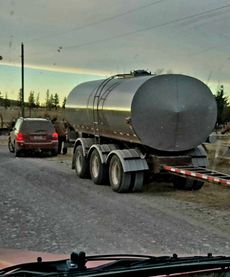 A tanker truck blocking a road, with a red car stopped behind it.