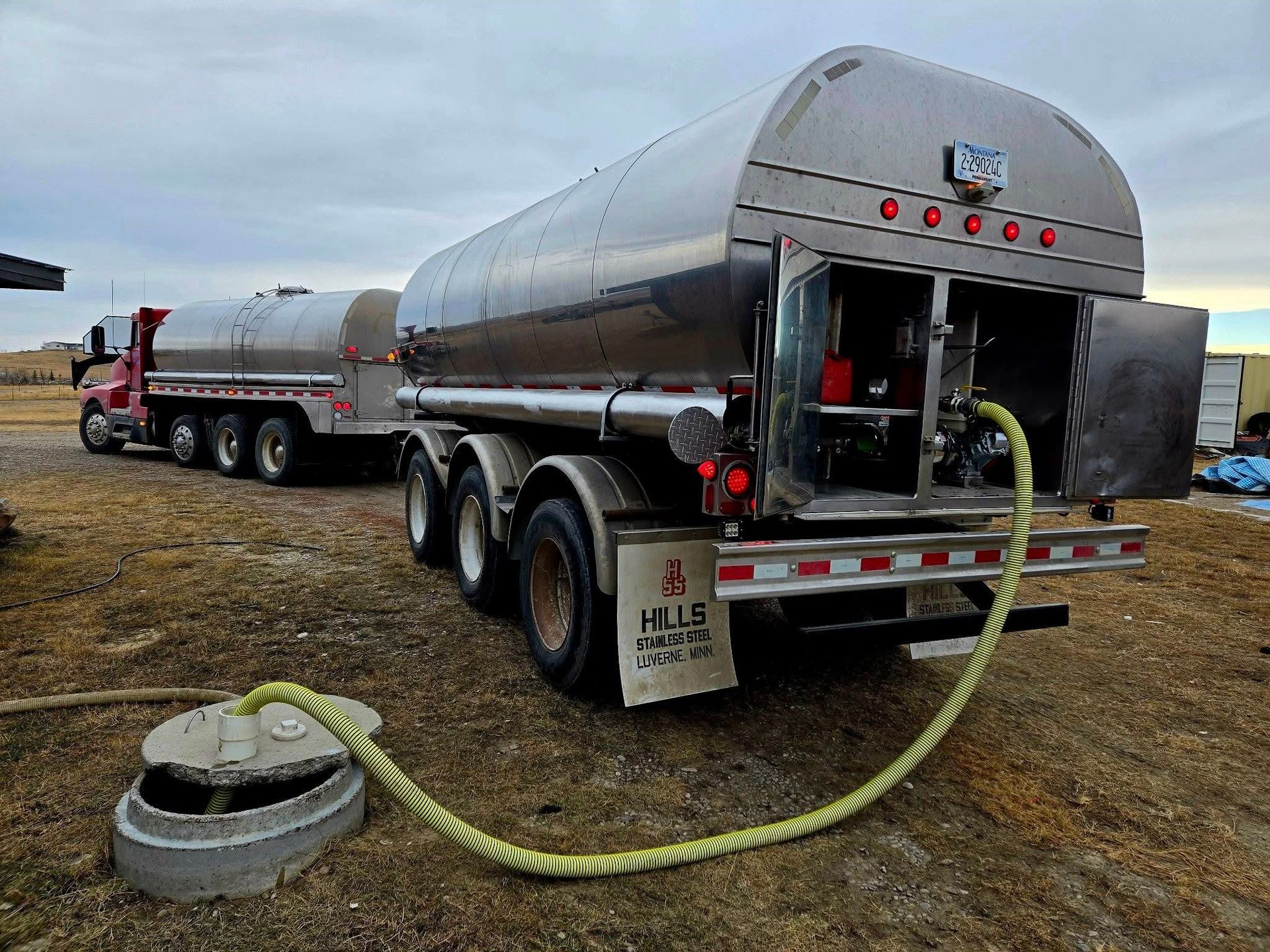 Fuel tanker truck unloading fuel through a hose into a concrete underground tank.