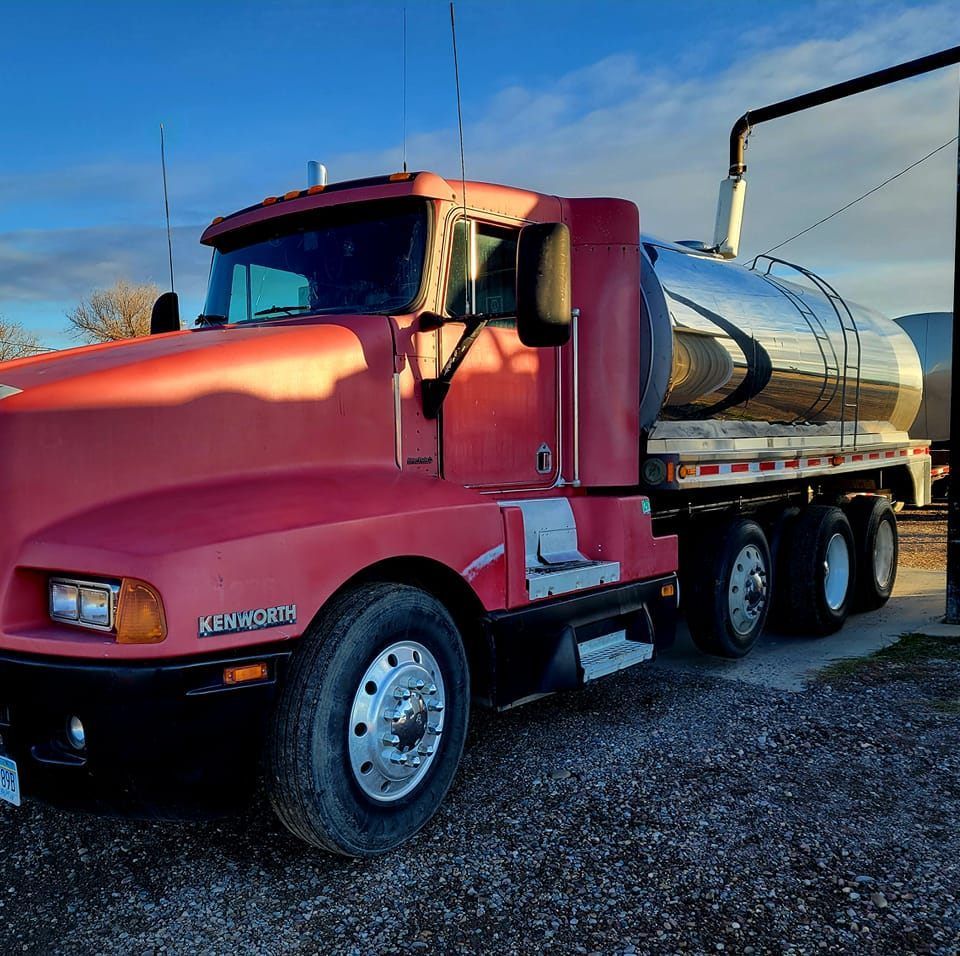 Red Kenworth tanker truck parked outdoors, shiny silver tank, blue sky.