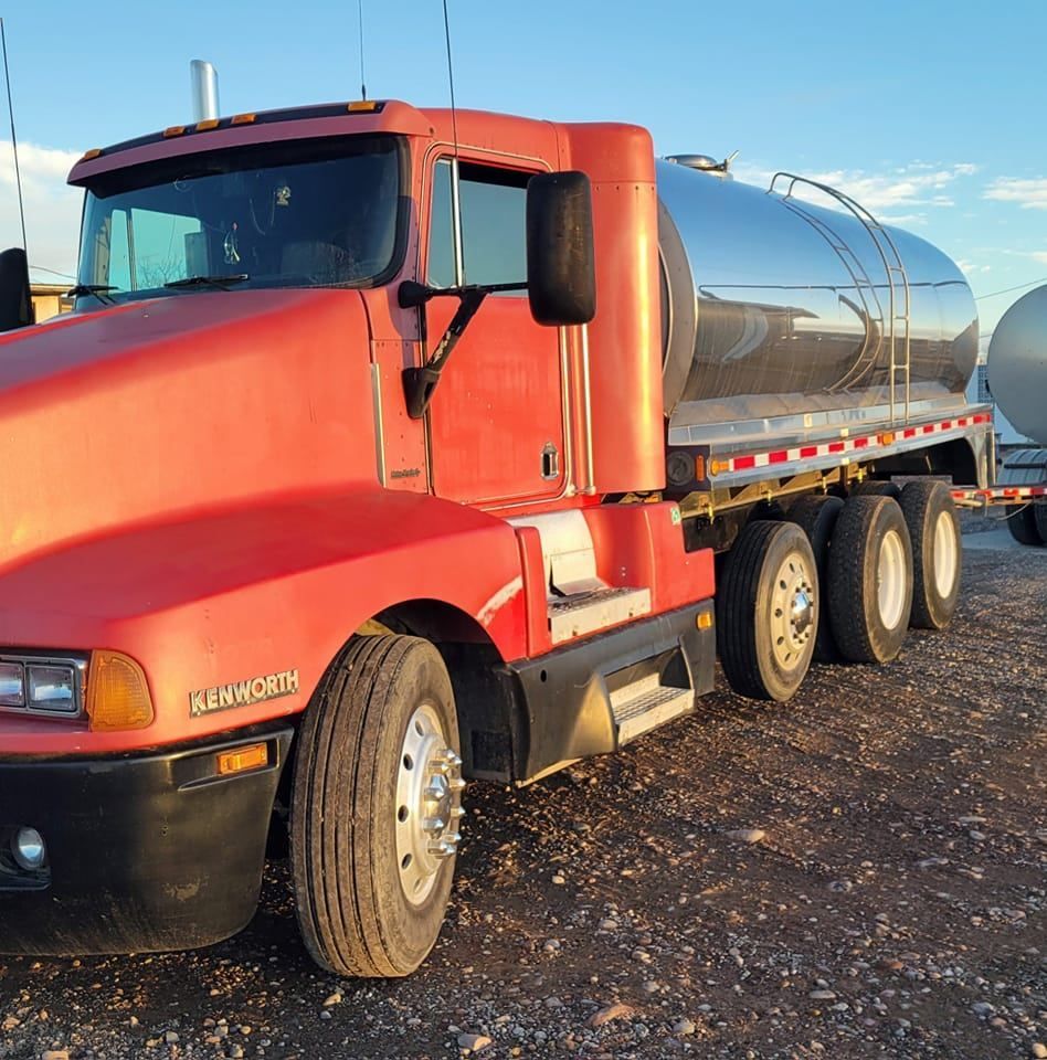 Red Kenworth tanker truck parked outdoors on gravel.