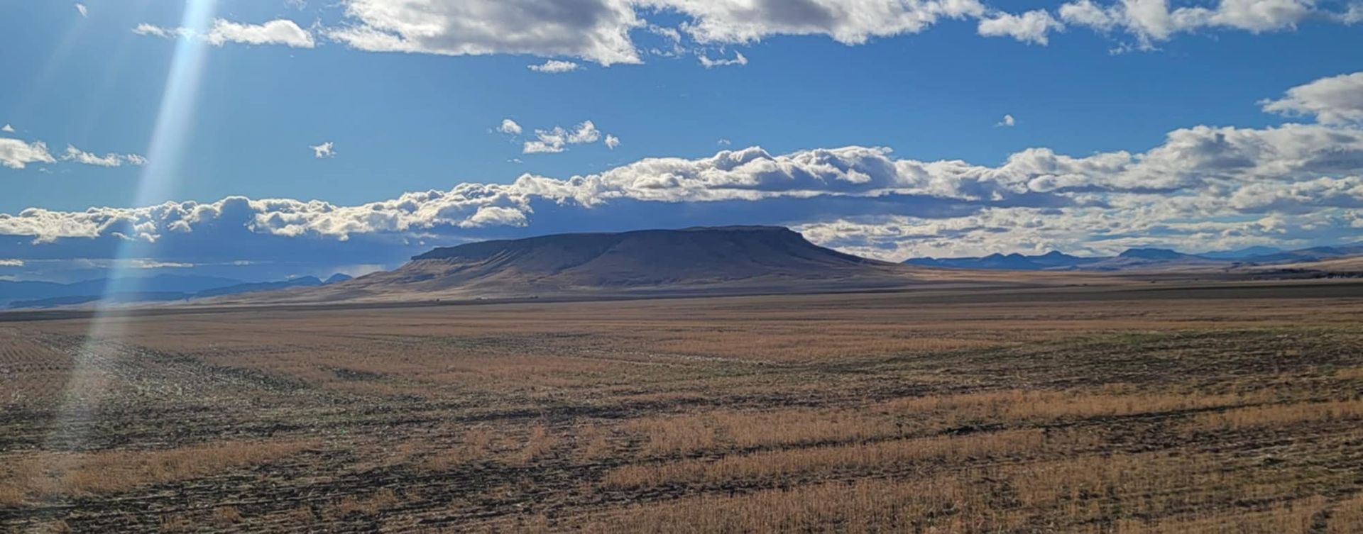 Open landscape with a flat-topped mountain under a partly cloudy sky, sunlight streaks across the scene.