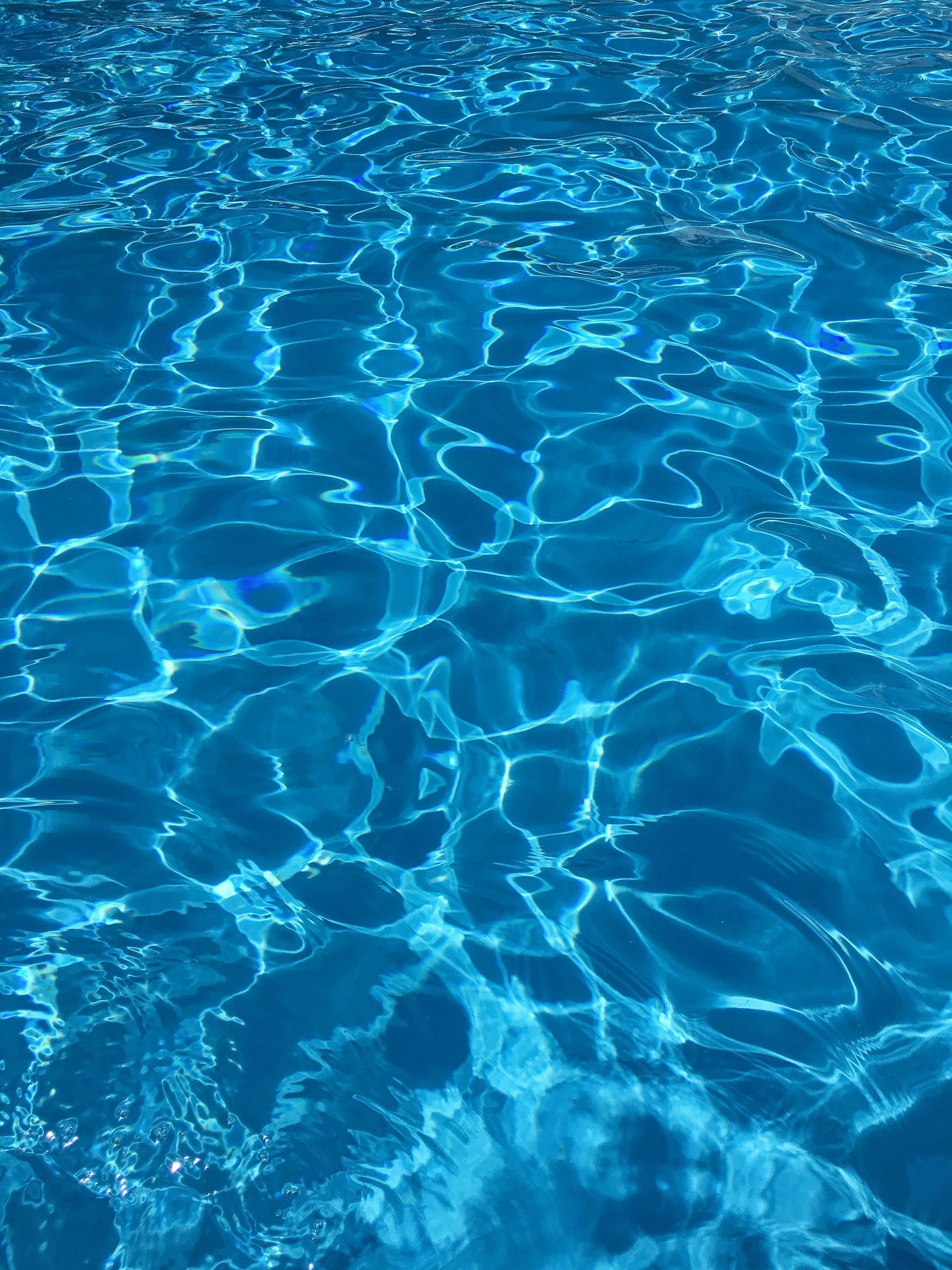 Bright blue water in a pool reflecting sunlight, with rippling patterns and shadows.