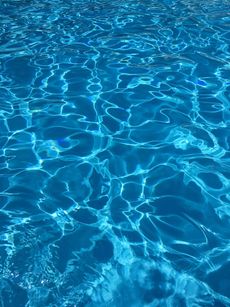 Bright blue water in a pool reflecting sunlight, with rippling patterns and shadows.