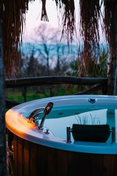 Hot tub outdoors, wooden frame, water reflecting the sky, faucet with a towel.