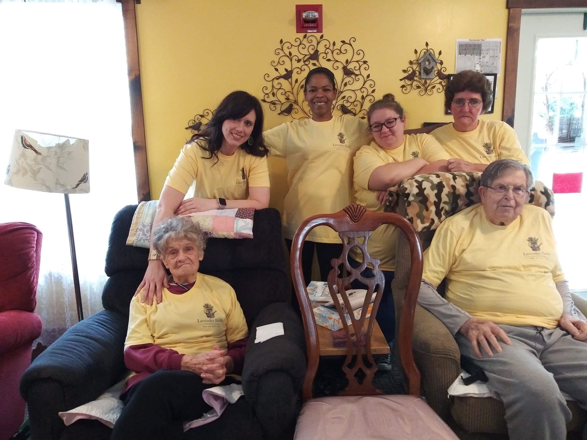 Group of people in yellow shirts, smiling, posing together in a room with yellow walls.
