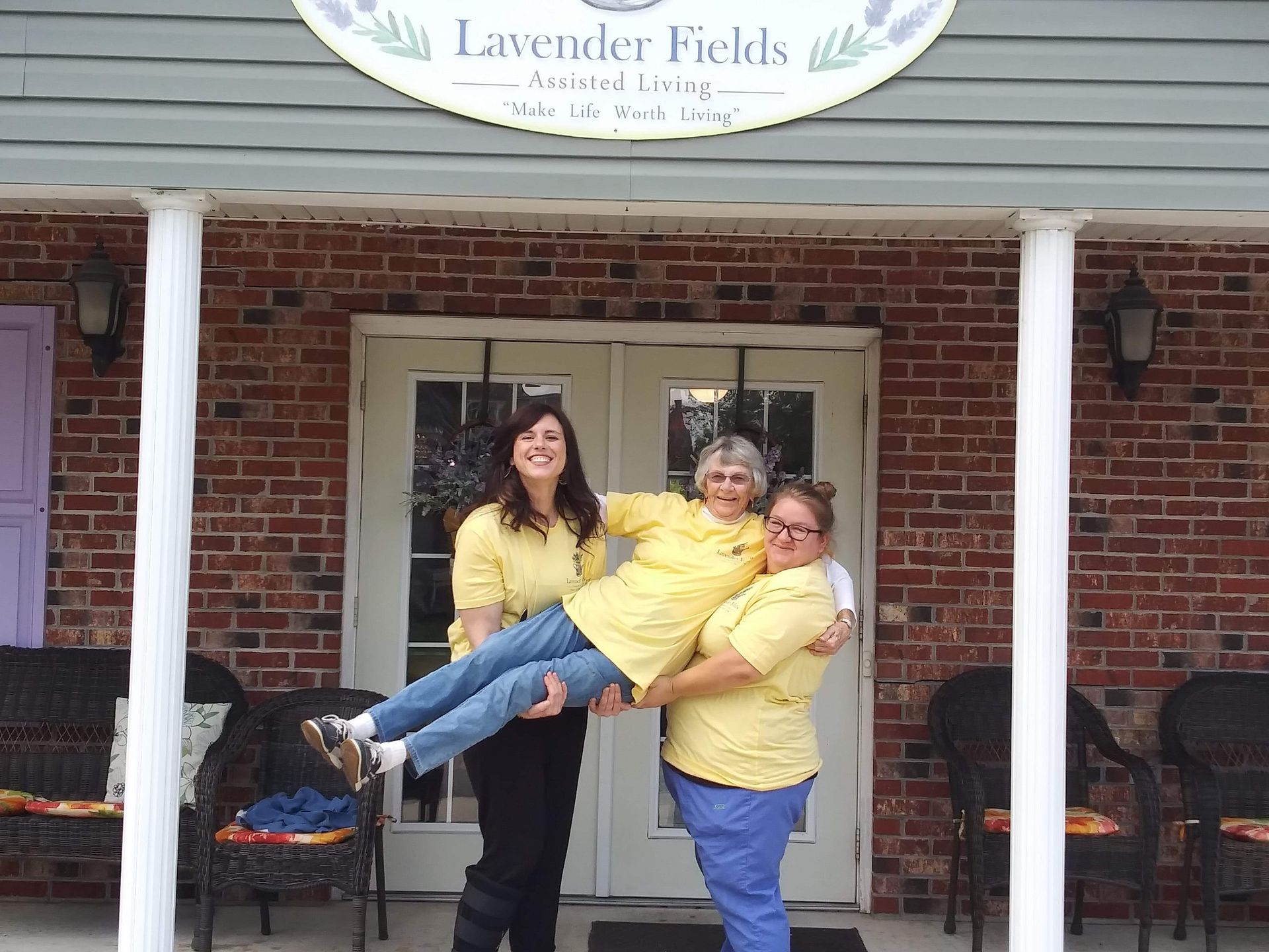 Three women holding up another smiling in front of a building, 