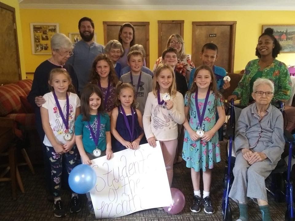 Group of children and adults holding a sign and medals indoors. Some smiling.
