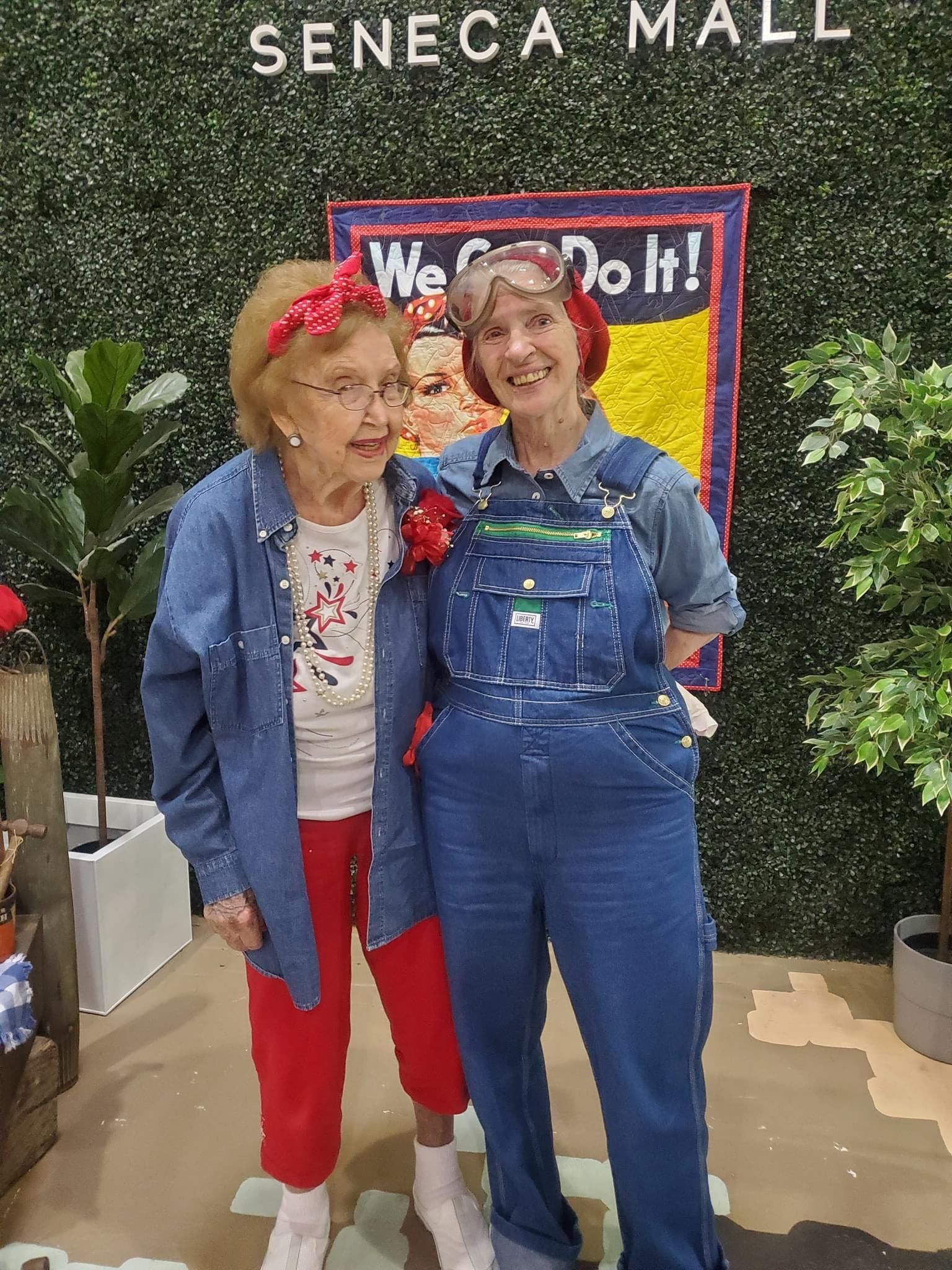 Two women posing at Seneca Mall, one in denim overalls and the other in red, in front of a 