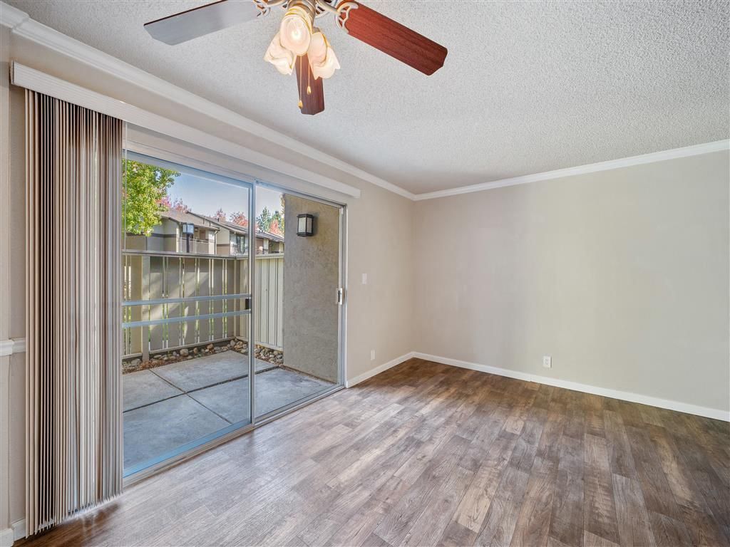 Empty living room with sliding glass door to a small patio, ceiling fan, and wood-look flooring.