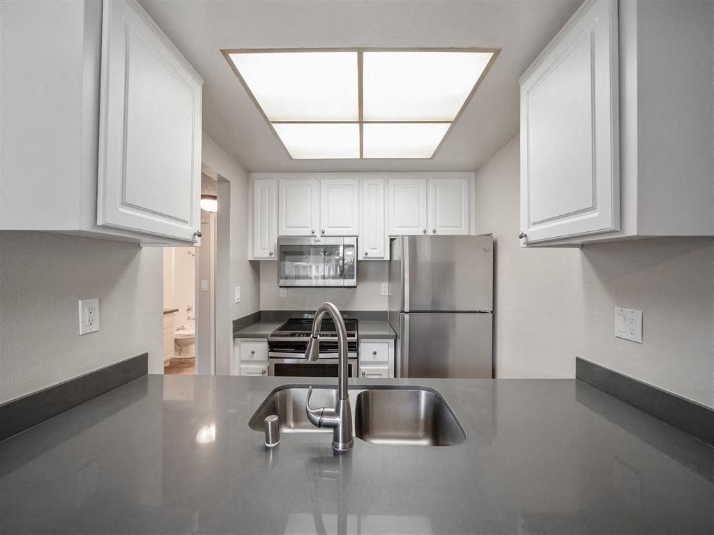 Kitchen in an apartment with white cabinets, stainless steel appliances, and a centered sink.