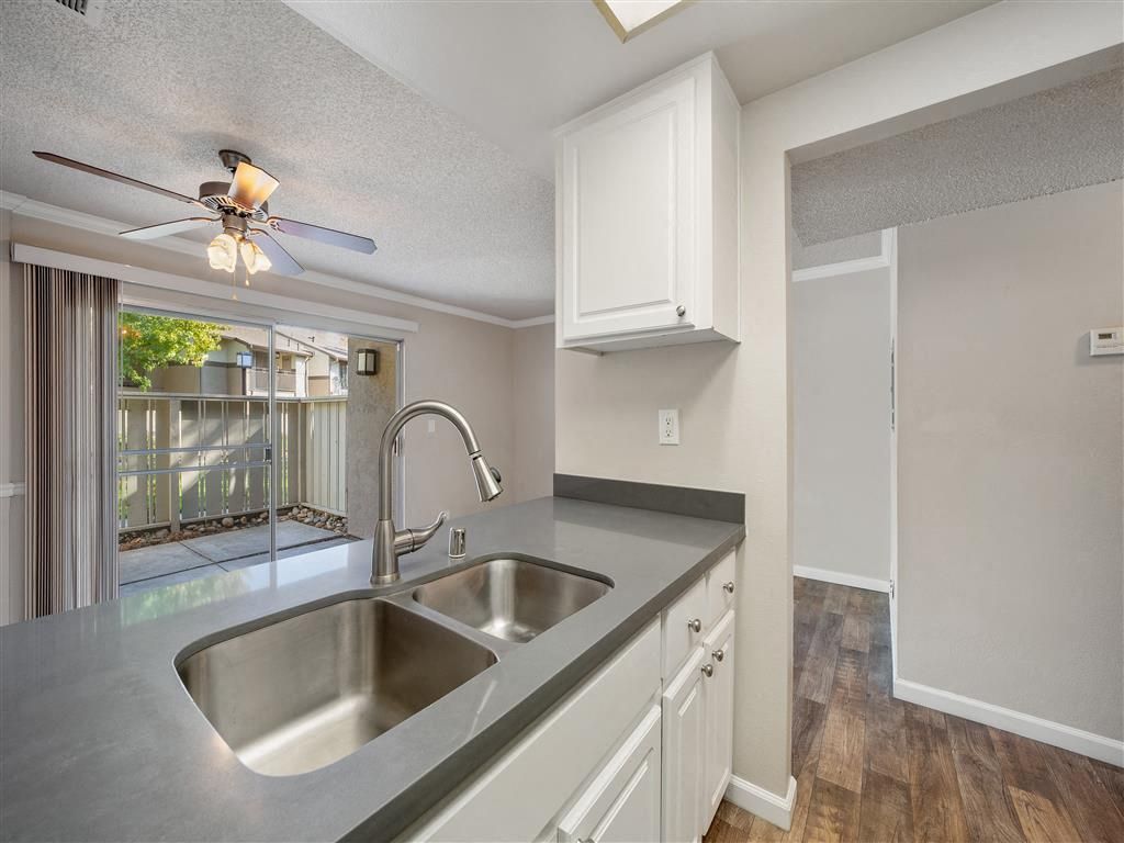 Kitchen with double sink, gray countertops, white cabinets, and a sliding glass door to the patio.