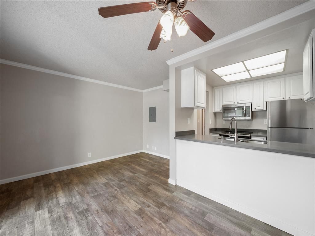 Open-concept kitchen and living area with white cabinets, stainless steel appliances, and a ceiling fan.