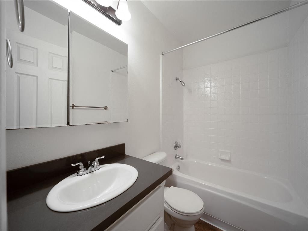 Bathroom with white tile tub/shower, sink, mirror, and toilet.