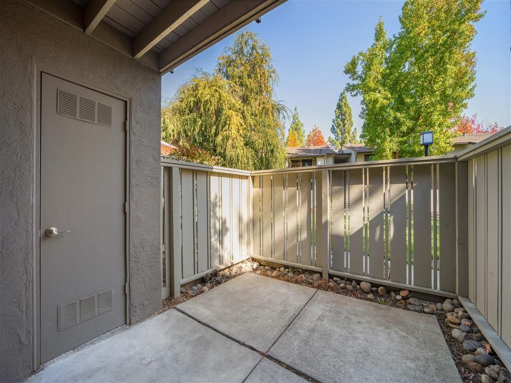 Concrete patio with beige railing and a back door of a ground-floor apartment.