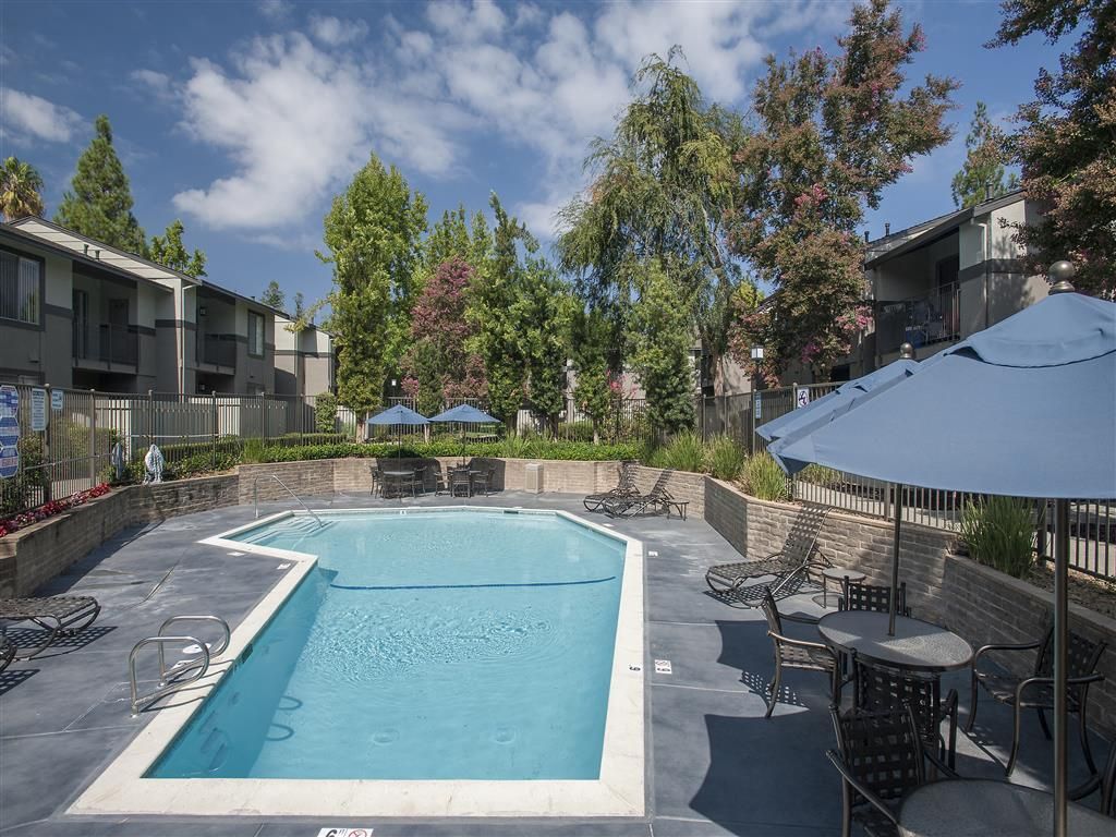 Outdoor apartment community pool with lounge chairs and umbrellas.