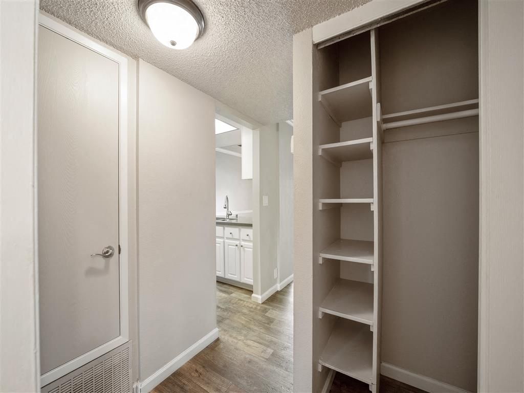 Hallway of an apartment featuring a built-in closet with shelves and a view into the kitchen.