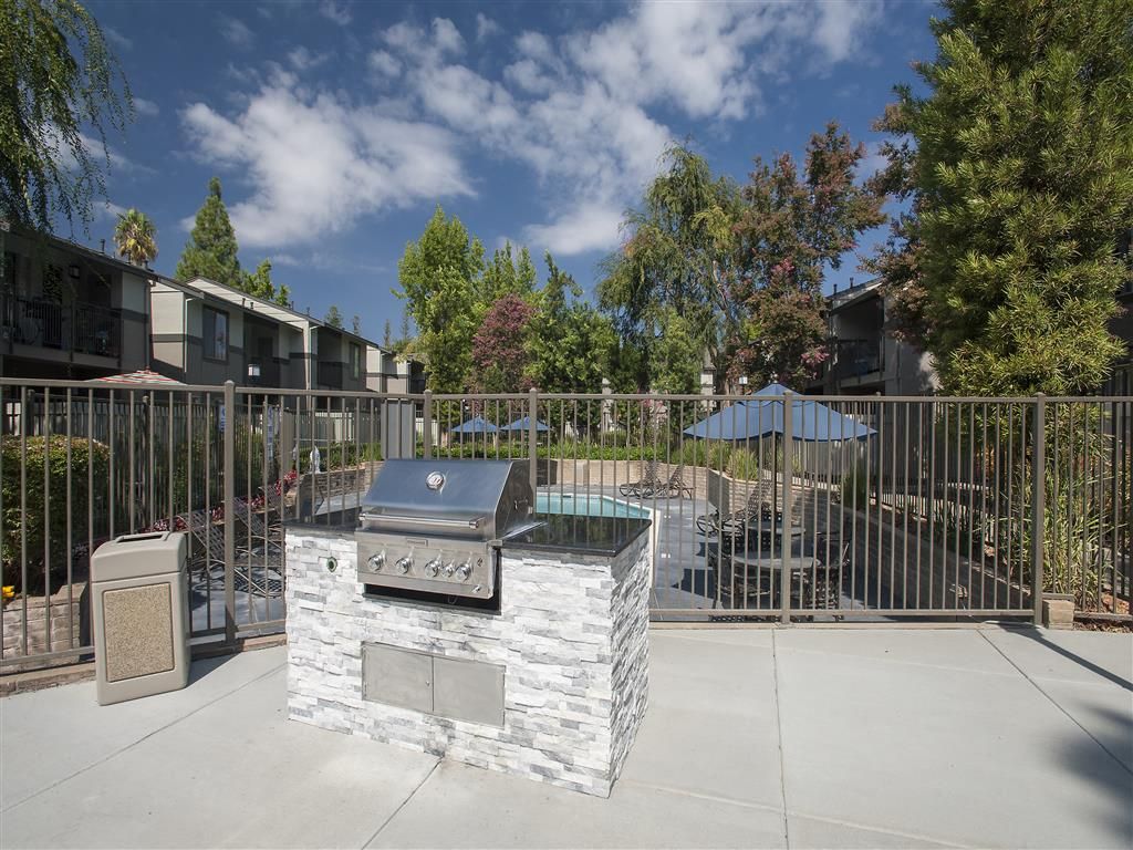 Outdoor communal BBQ grill area with a fenced pool and lounge seating.