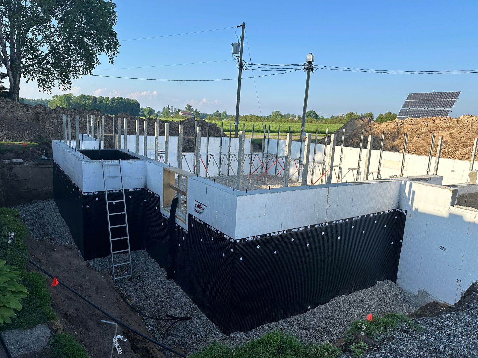 A construction site of an ICF foundation. The stone slinger has brought in the stones. The waterproofing is complete.