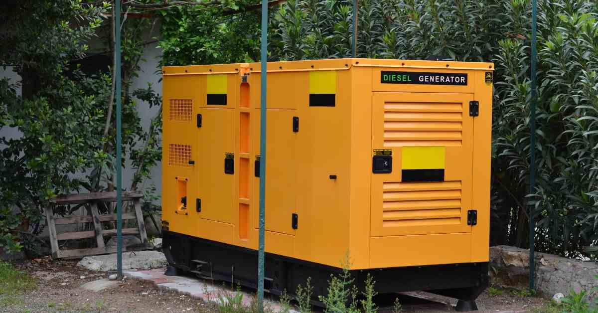 A yellow, rectangular whole-home generator powered by diesel sits on a concrete slab in front of tal