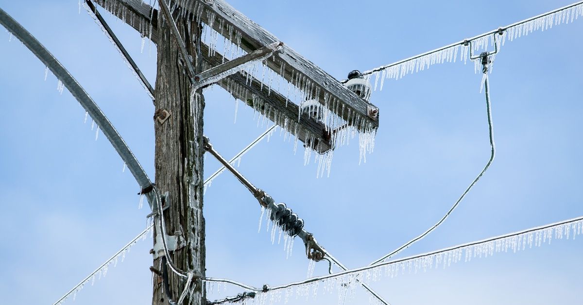 A wooden utility pole and power lines are heavily coated in ice against a clear blue sky.