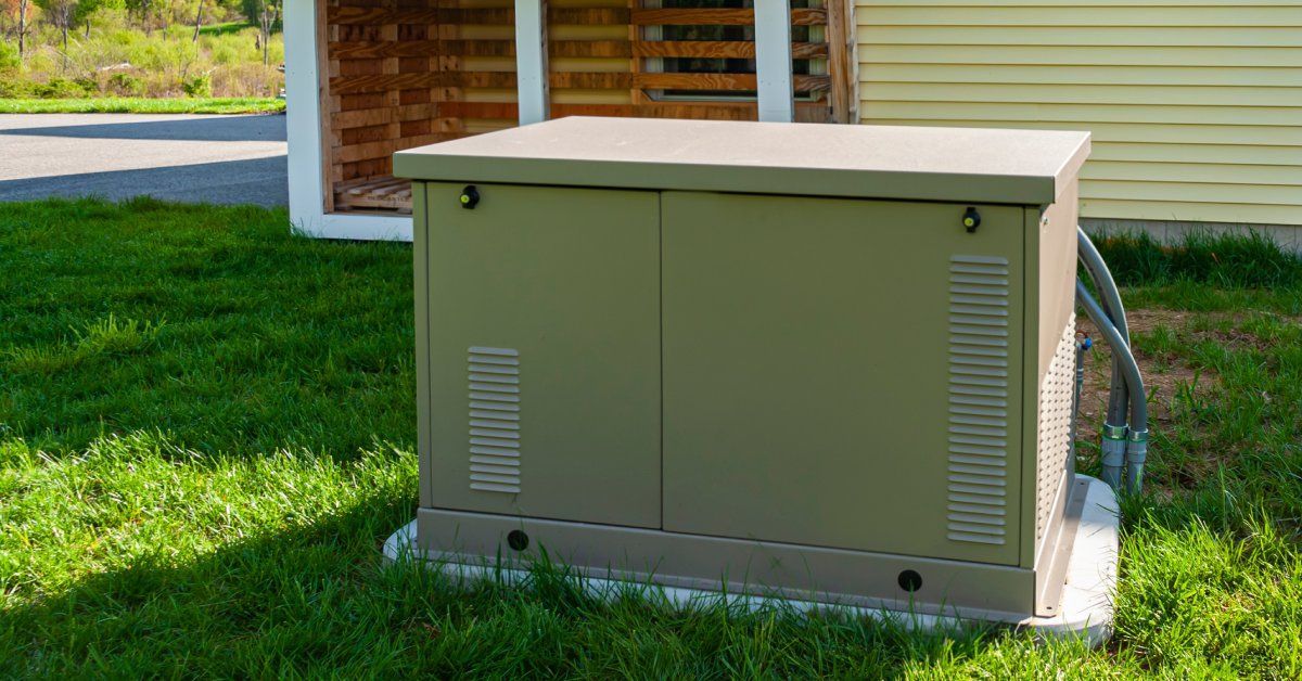 A generator is several feet away from the side of a house. The house has yellow siding.